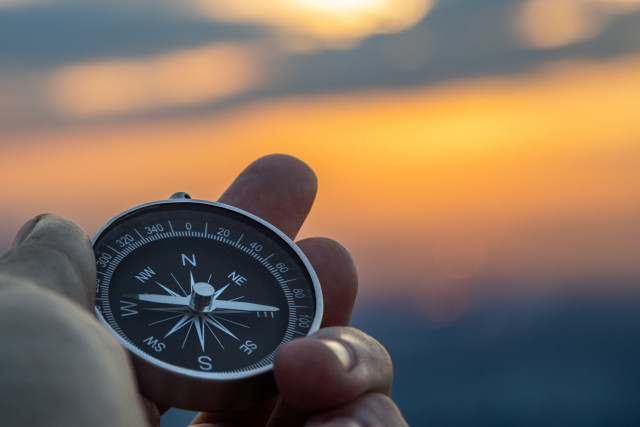 Compass in person's hand with sunset in the background