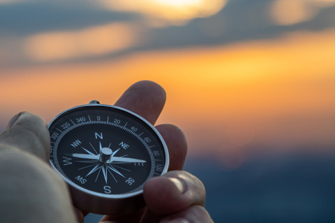 Compass in person's hand with sunset in the background